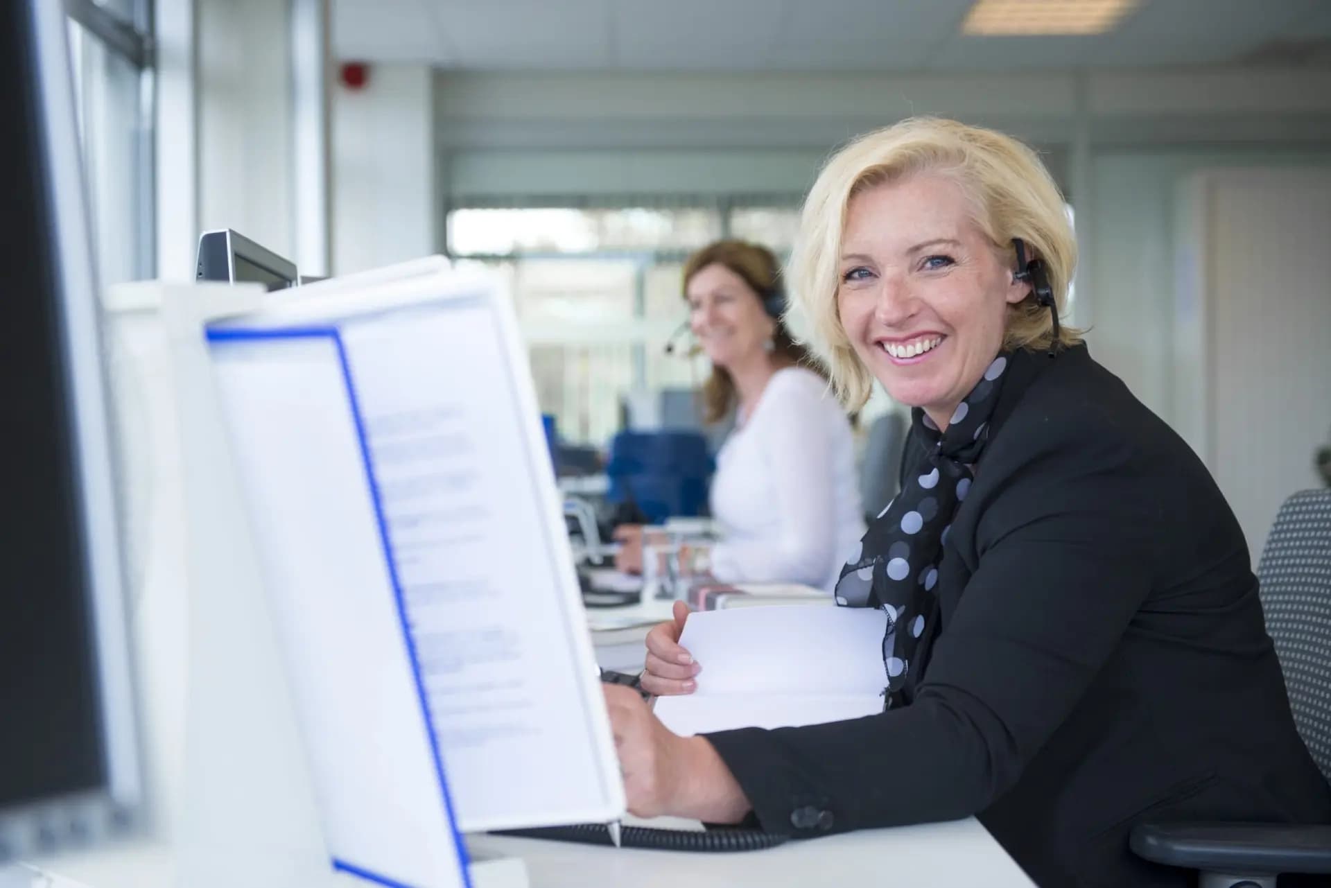afbeelding van een mevrouw aan een bureau met een headset op, kantoor De Nationale Adviesbalie